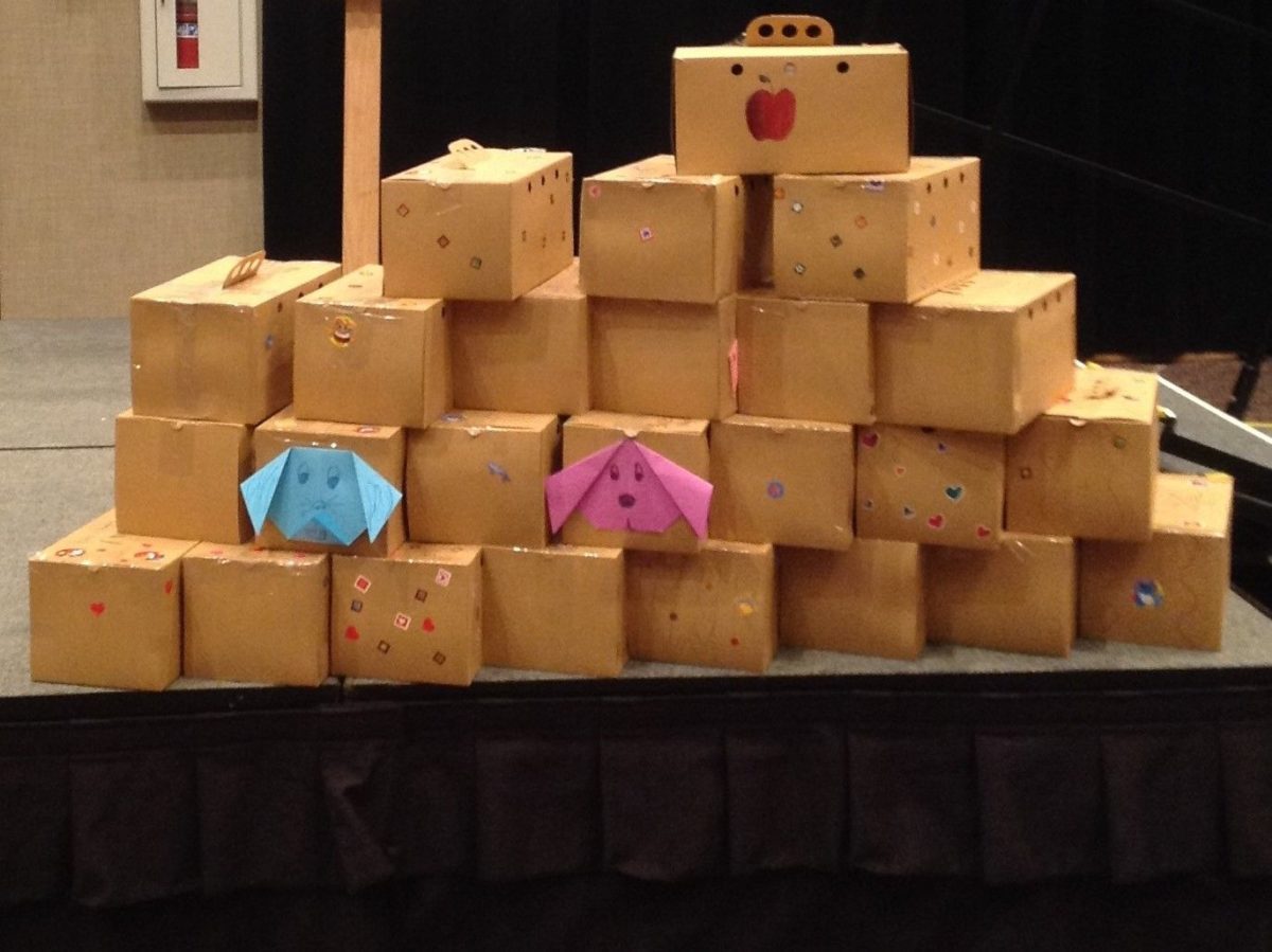 photo of a stack of care package boxes stacked up with a couple paper fold craft dog faces on 2 boxes, one blue one pink